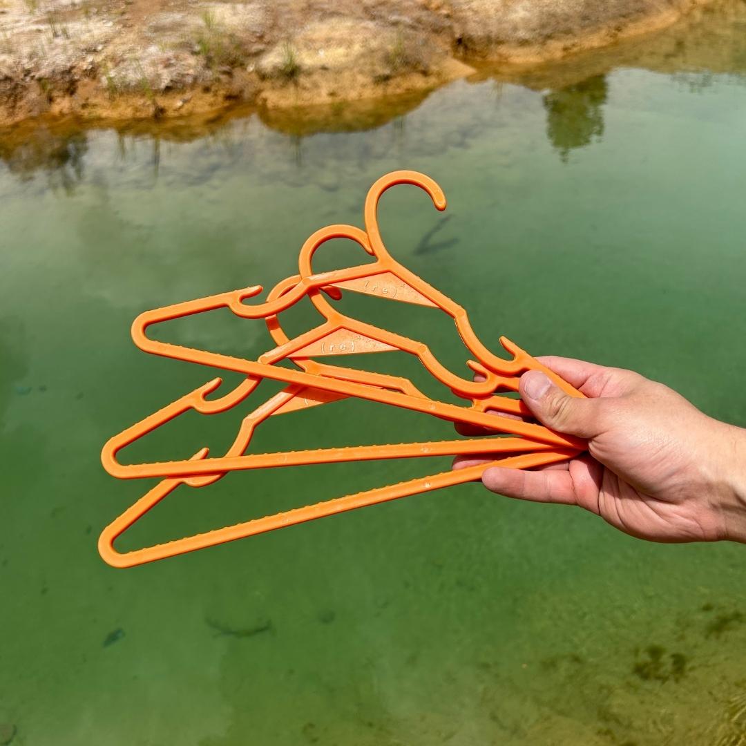 three orange ( r e ) ˣ hangers held over a green clean body of water